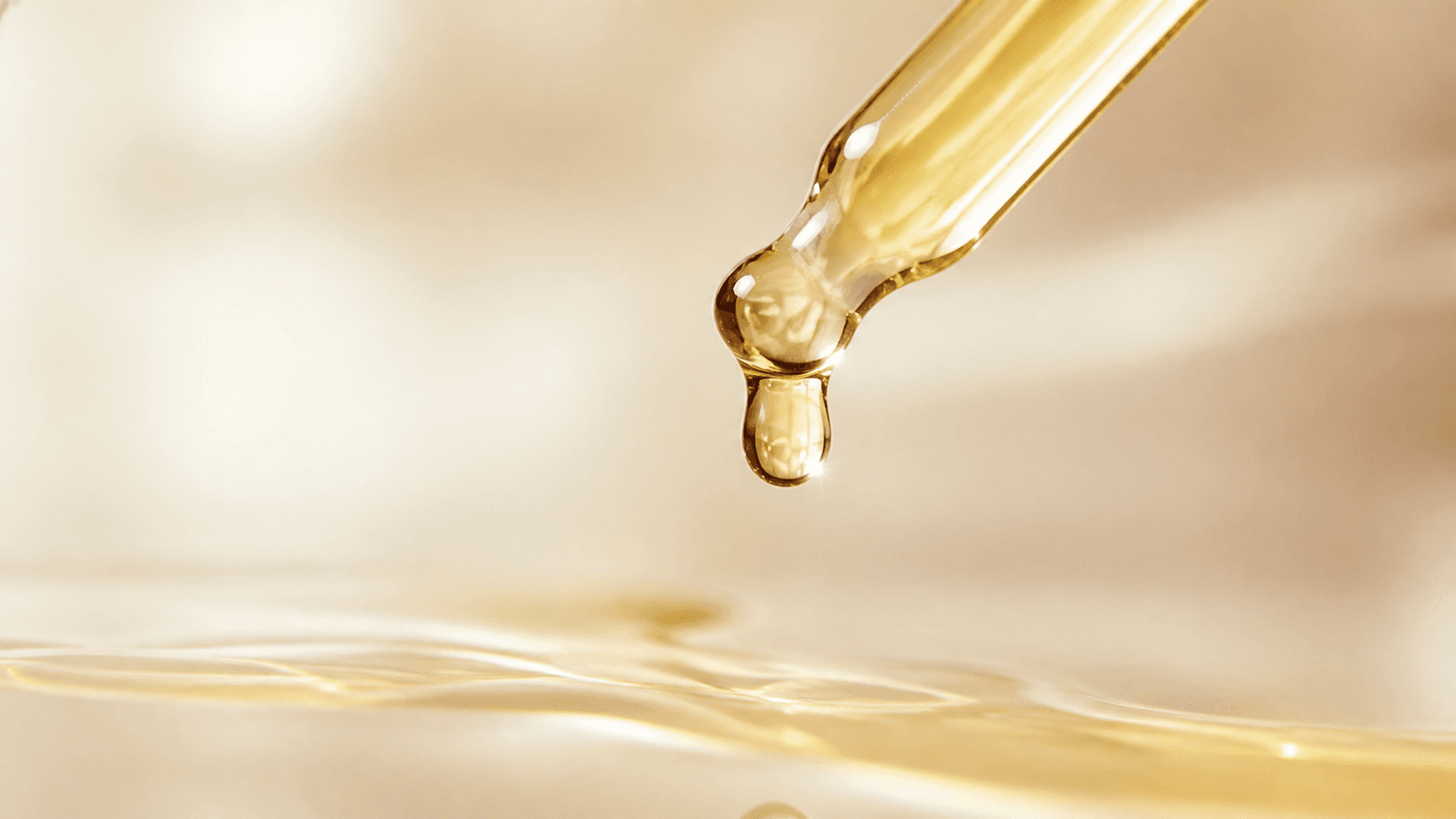 A glass dropper releasing a single golden droplet of jojoba oil, showing the lightweight glide jasclair recommends